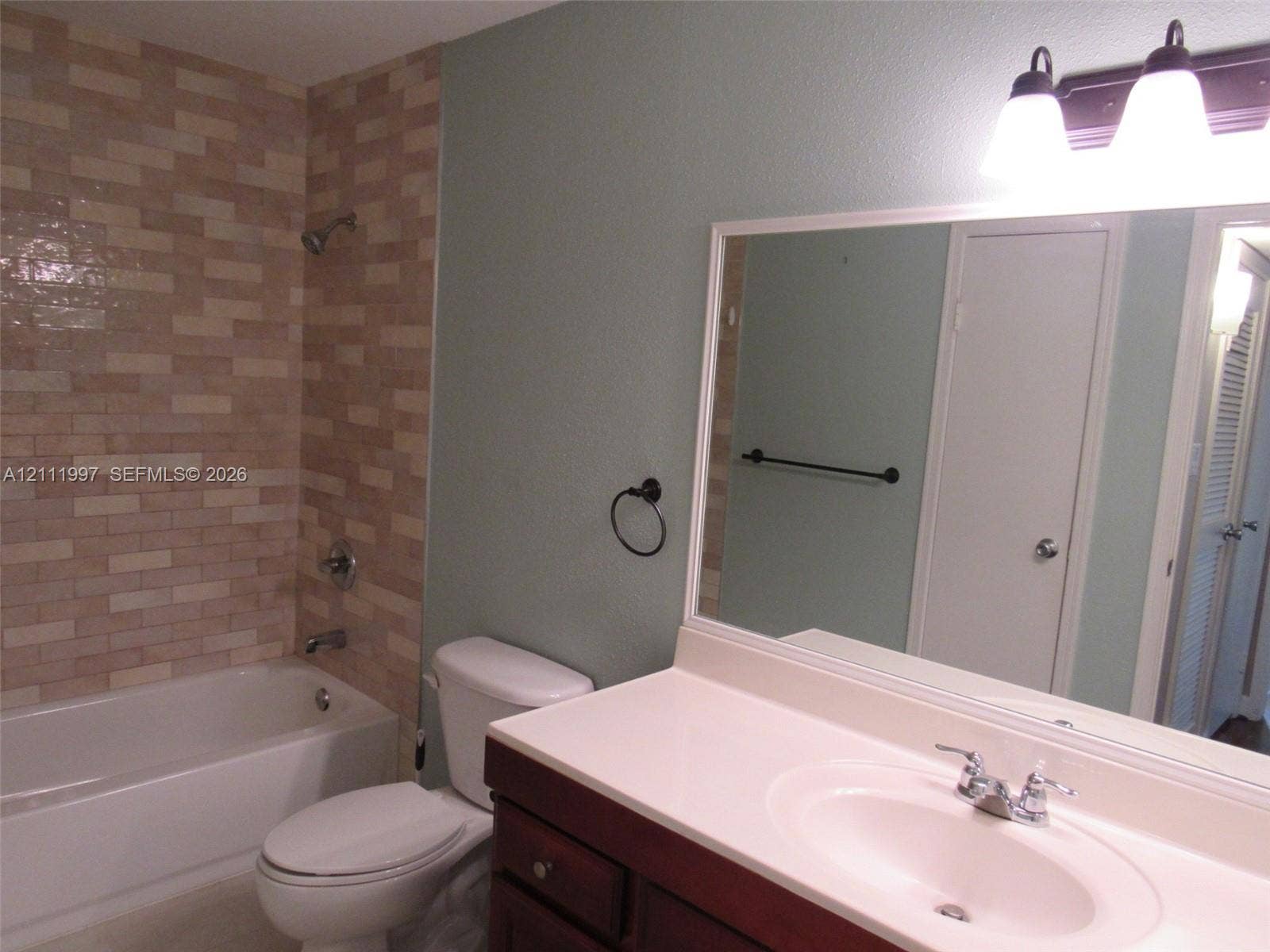 733 Riverside Drive, #1232, Coral Springs, Coral Springs, FL 33071 Bathroom featuring a shower and bathtub combination with rectangular tile surround, dark wood vanity, solid-surface countertop with an integrated sink, and triple-bulb wall-mounted vanity lighting