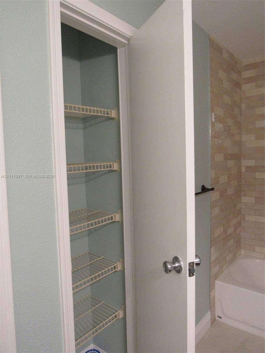 733 Riverside Drive, #1232, Coral Springs, Coral Springs, FL 33071 Built-in storage closet featuring five wire shelving tiers, complemented by a matte black towel bar and textured stone-finish wall tile surrounding the bathtub