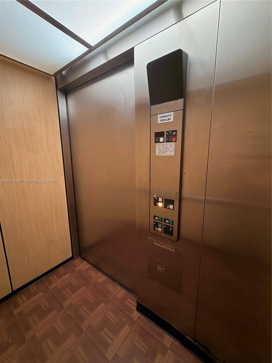 733 Riverside Drive, #1232, Coral Springs, Coral Springs, FL 33071 Elevator interior featuring brushed stainless steel panels, wood-finish wall paneling, parquet flooring, and an integrated ceiling lighting panel