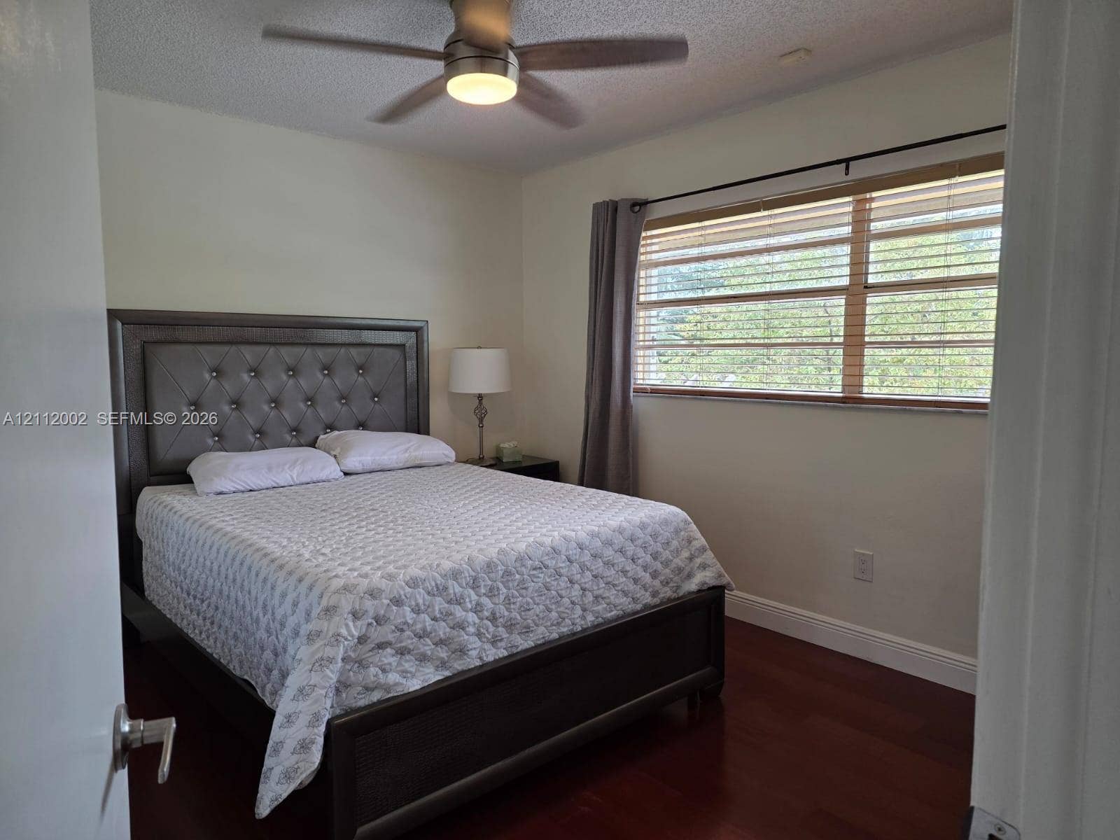 Room featuring dark wood-finish flooring, a ceiling fan with integrated lighting, and a window with horizontal blinds