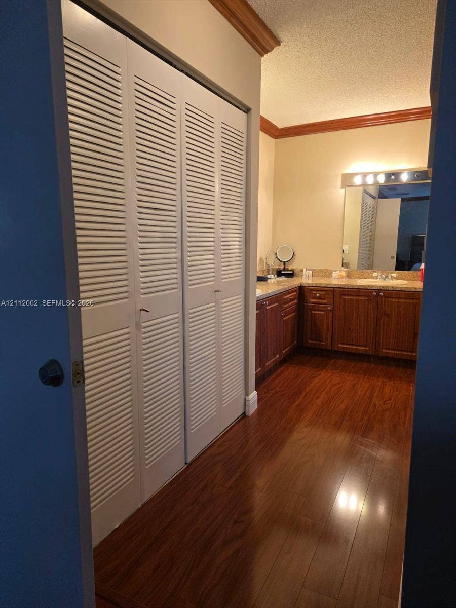 Wood-finish flooring, white louvered bifold closet doors, dark wood-finish cabinetry, stone-finish countertop, and wall-mounted vanity lighting
