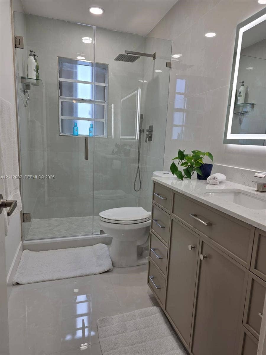 Walk-in shower with frameless glass enclosure, rainfall showerhead, and integrated stone-style tile surround