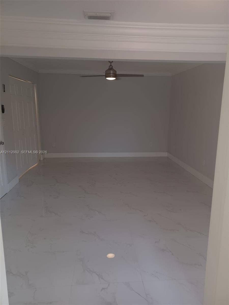 Neutral-toned interior space featuring large-format stone-patterned floor tile, crown molding, and a central ceiling fan