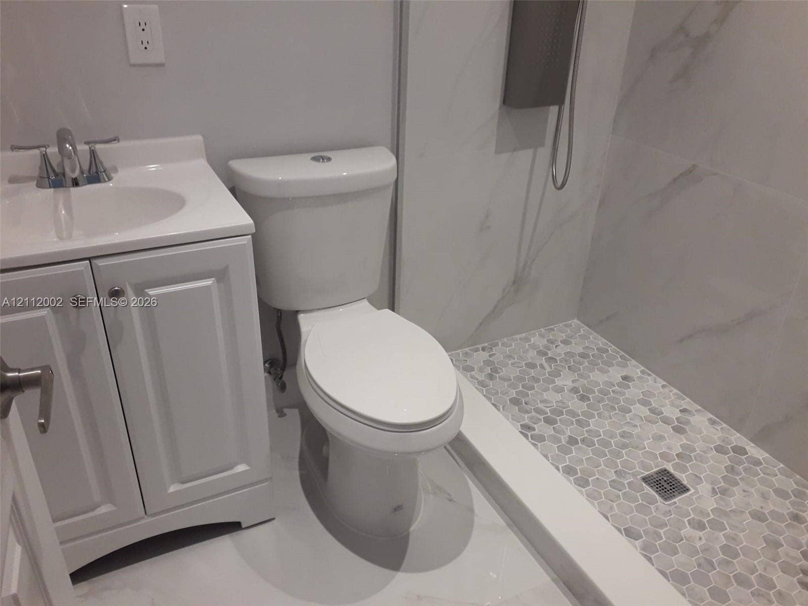 Bathroom featuring a white vanity cabinet with a integrated sink, two-piece toilet, and a walk-in shower with large-format wall tile and a hexagonal tile floor