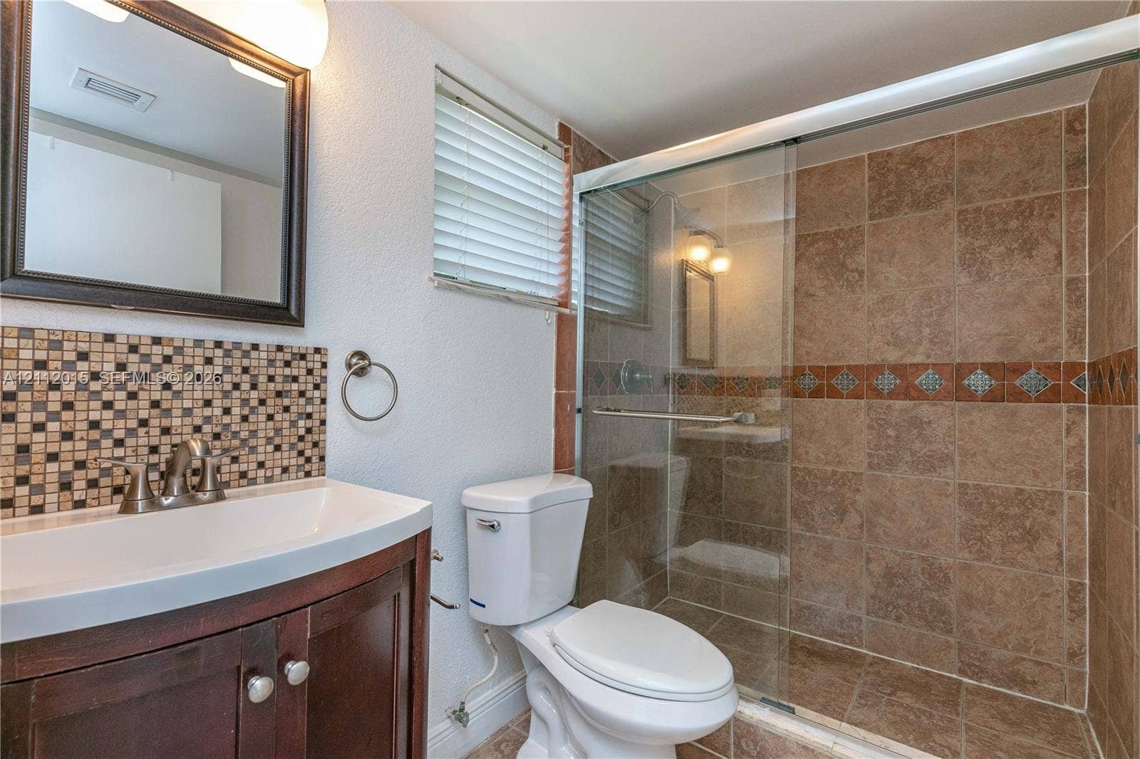 717 Gardens Drive, #201, Pompano Beach, Pompano Beach, FL 33069 Bathroom featuring a dark wood-finish vanity, decorative mosaic tile backsplash, framed wall mirror, and walk-in shower with glass enclosure and tiled surround
