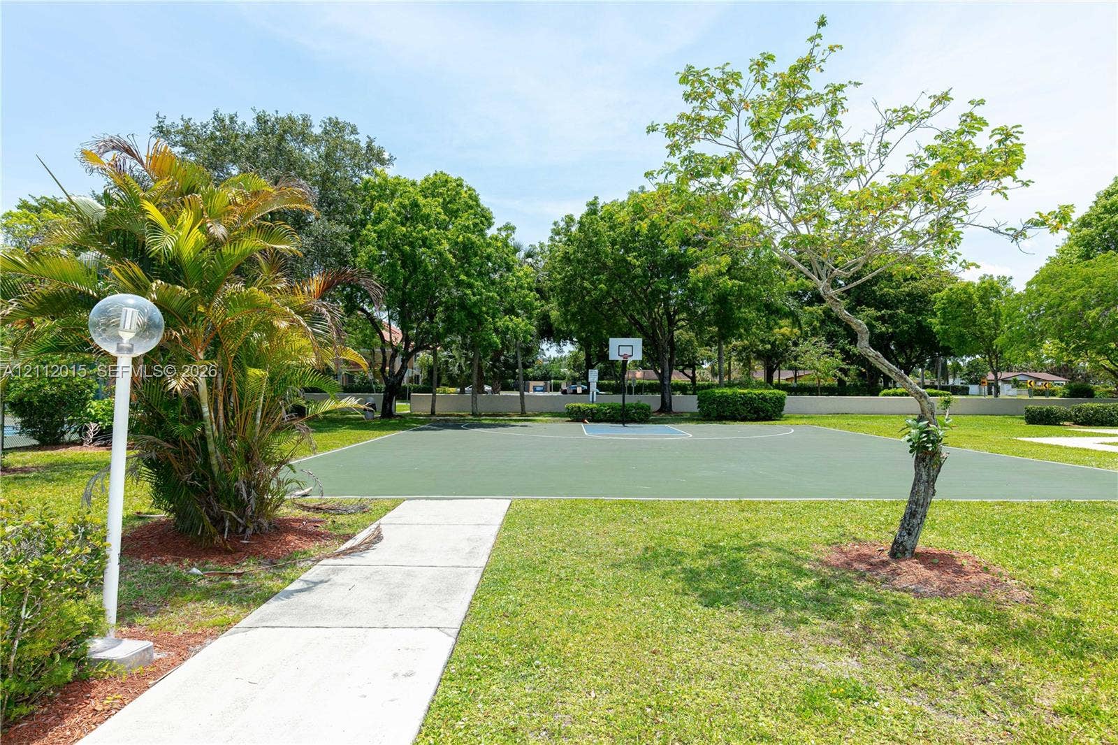 717 Gardens Drive, #201, Pompano Beach, Pompano Beach, FL 33069 Outdoor recreation area featuring a paved basketball court, concrete pedestrian walkway, manicured lawn, established trees, and globe-style lighting