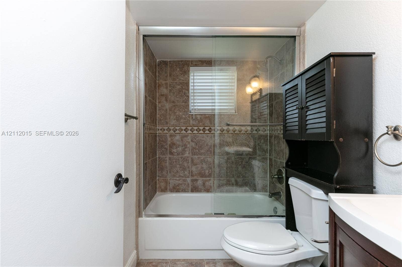 717 Gardens Drive, #201, Pompano Beach, Pompano Beach, FL 33069 Bathtub with glass sliding enclosure, tile wall surround with decorative accent inlay, built-in over-the-toilet storage cabinet, and wall-mounted towel ring