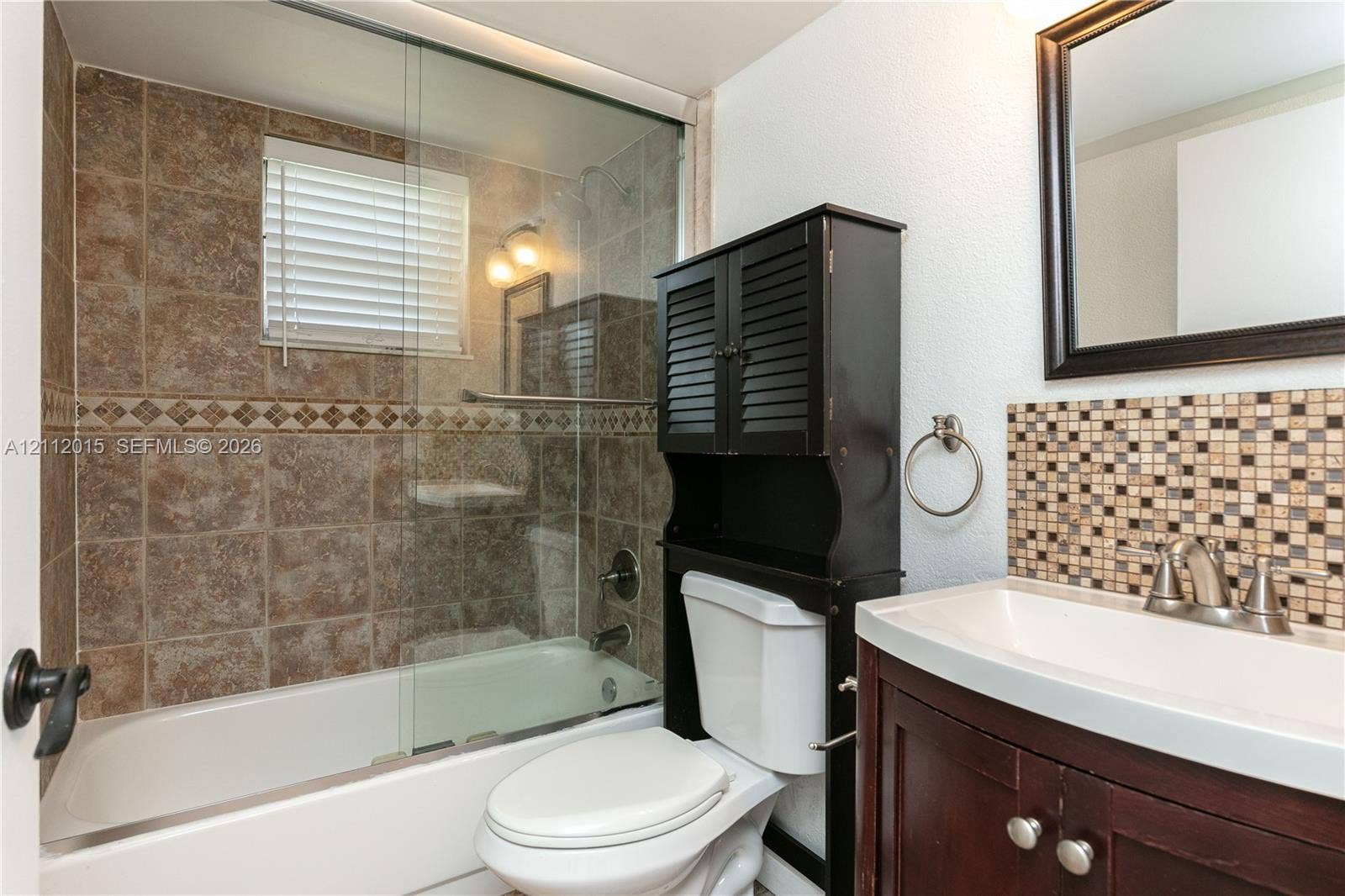 717 Gardens Drive, #201, Pompano Beach, Pompano Beach, FL 33069 Bathroom featuring a shower-tub combination with glass enclosure, tiled surround with decorative accent border, mosaic tile backsplash, dark wood-finish vanity, and wall-mounted mirror