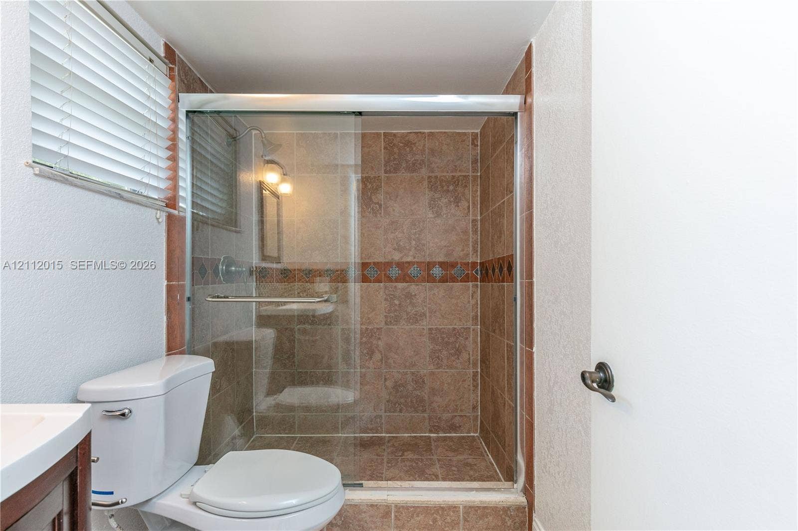 717 Gardens Drive, #201, Pompano Beach, Pompano Beach, FL 33069 Walk-in shower featuring glass sliding doors and decorative tile inlay, ceramic tile wall finishes, and a neutral-tone commode