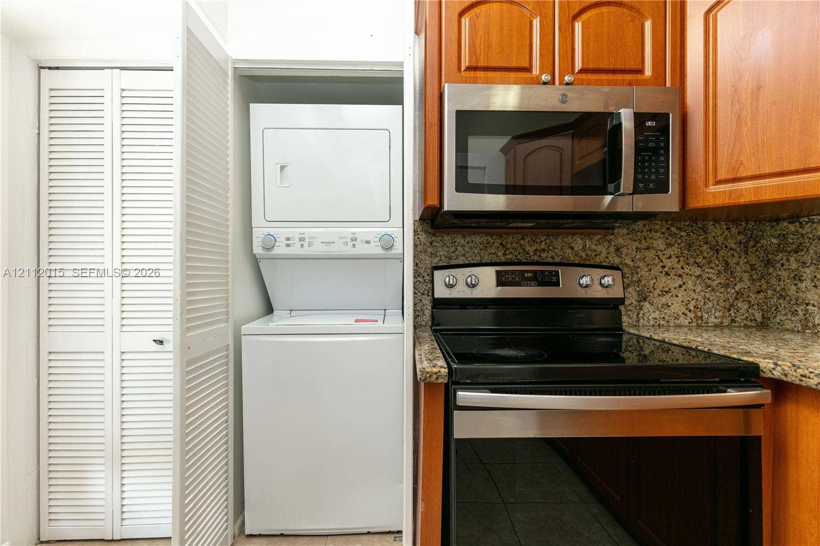 717 Gardens Drive, #201, Pompano Beach, Pompano Beach, FL 33069 Stacked laundry center with white cabinetry doors, stone-finish countertops, natural wood-finish cabinetry, and stainless steel kitchen appliances