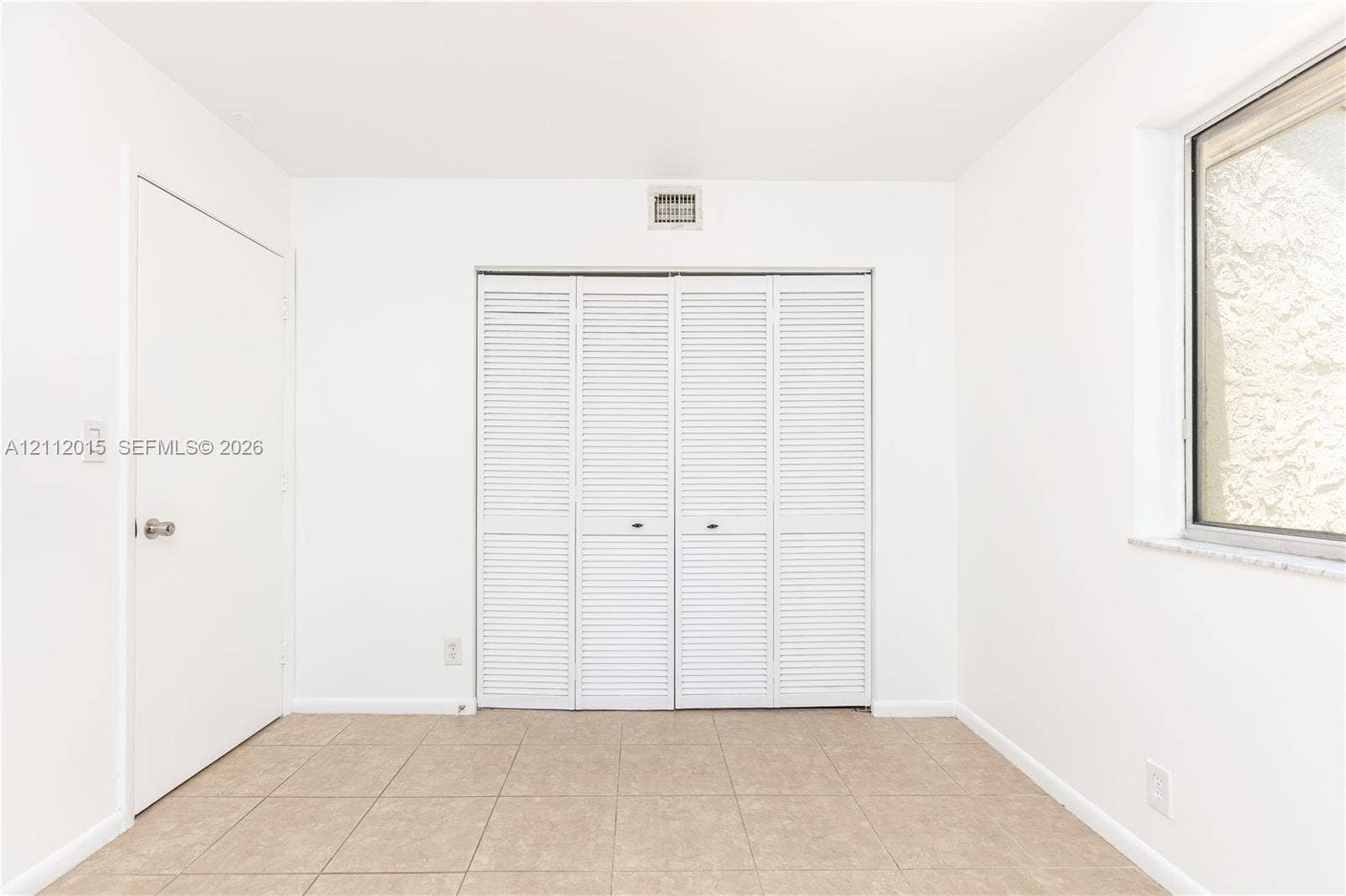 717 Gardens Drive, #201, Pompano Beach, Pompano Beach, FL 33069 Neutral interior space featuring tile flooring, a multi-panel closet with louvered doors, a solid-panel door, and a window with a stone sill