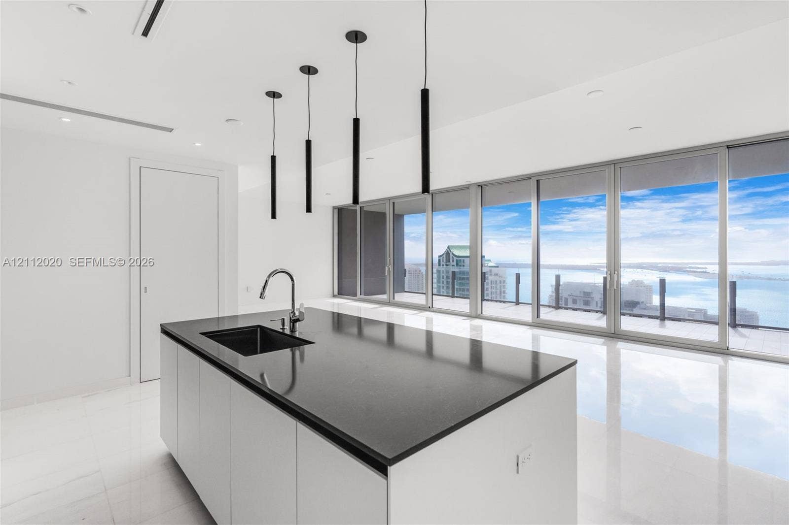 300 Biscayne Blvd Way, #4202, Miami, Miami, FL 33131 Center island featuring a dark stone countertop, integrated sink, and matte black faucet, complemented by minimalist pendant lighting and floor-to-ceiling glass sliding doors