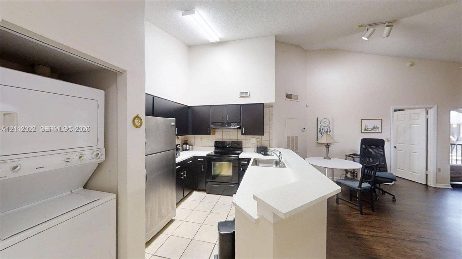 Kitchen featuring dark cabinetry, stainless steel appliances, ceramic tile flooring, a peninsula with counter seating, and vaulted ceilings