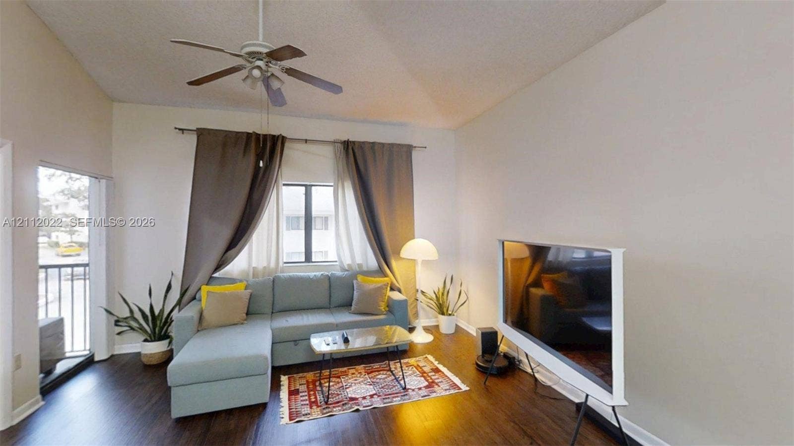 Vaulted ceiling with a central paddle ceiling fan, wood-finish flooring, and a sliding glass door providing external access