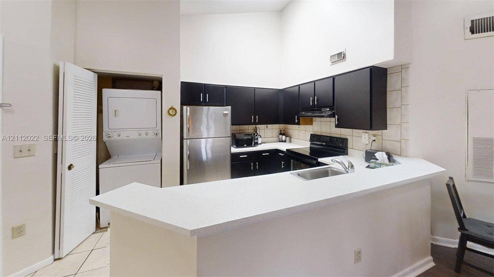 Kitchen featuring dark cabinetry, solid-surface countertops, stainless steel appliances, a recessed stainless steel sink, and a high-vaulted ceiling