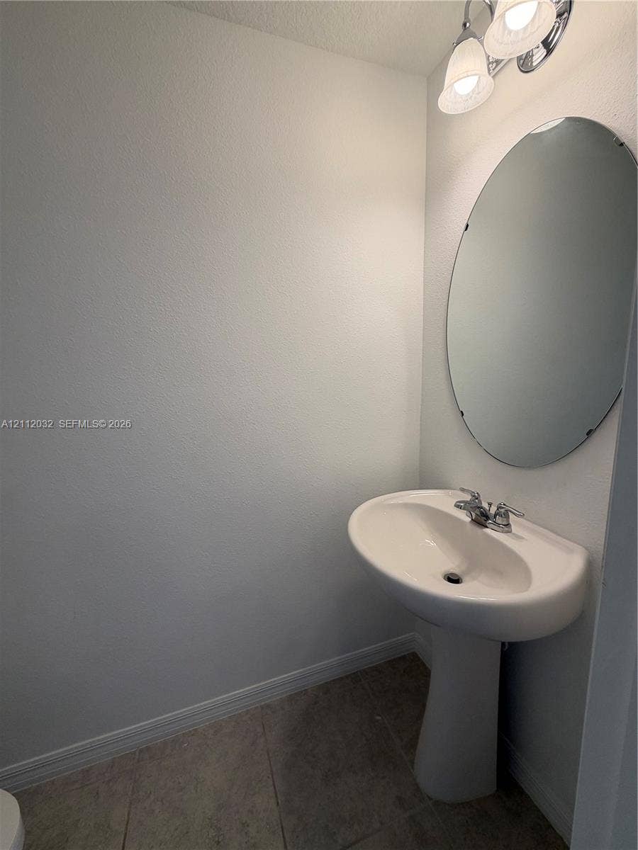 254 Mandovis Street, Davenport, Davenport, FL 33837 Pedestal sink with a dual-handle faucet, oval frameless wall mirror, and dual-globe light fixture