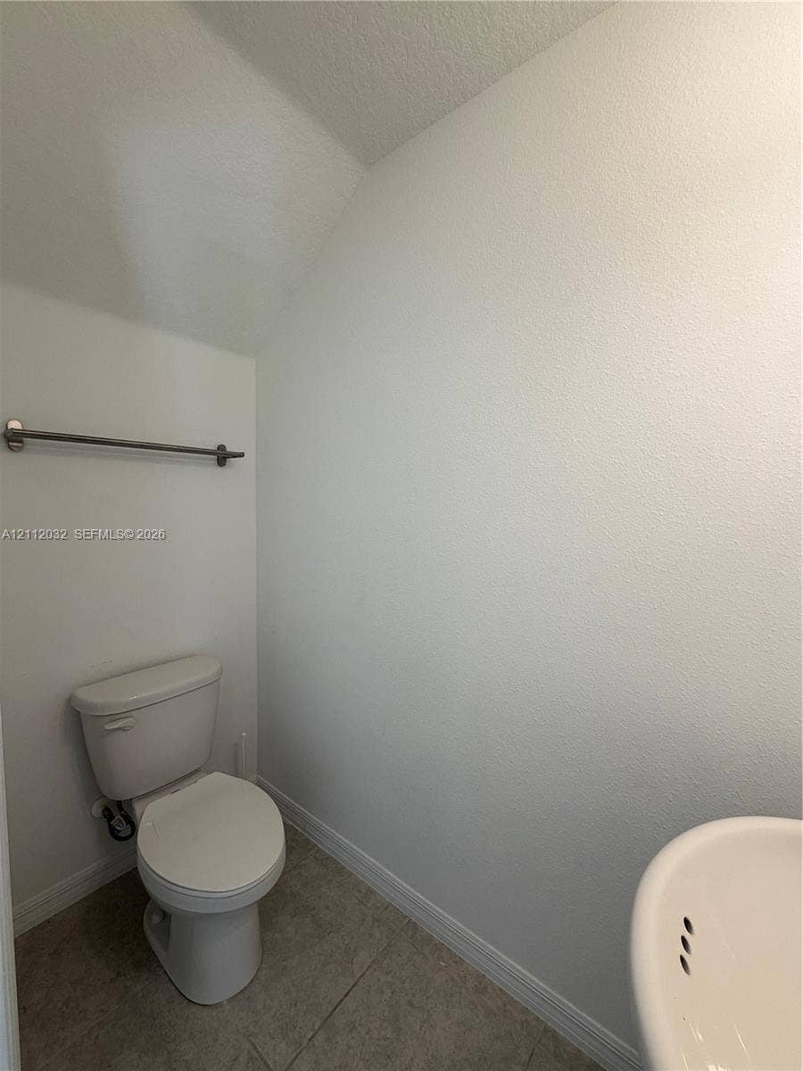 254 Mandovis Street, Davenport, Davenport, FL 33837 Powder room featuring a ceramic toilet, neutral tile flooring, and a wall-mounted metal towel bar