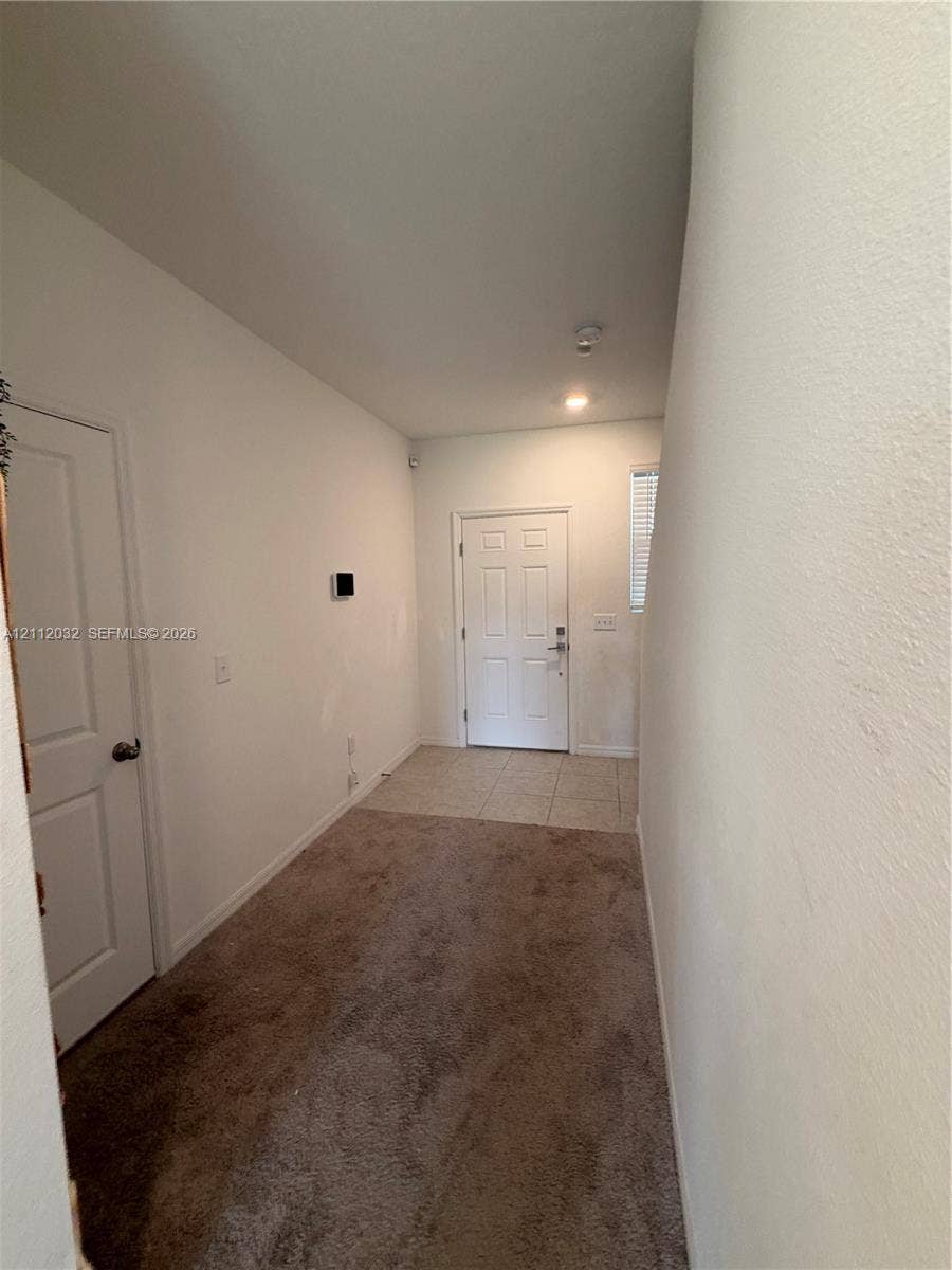254 Mandovis Street, Davenport, Davenport, FL 33837 Entryway featuring a white paneled front door, neutral wall-to-wall carpeting, and light-toned ceramic tile flooring