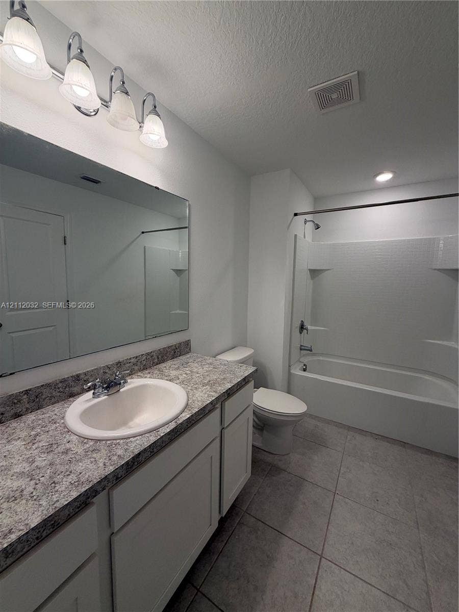 254 Mandovis Street, Davenport, Davenport, FL 33837 Bathroom featuring a vanity with stone-patterned countertop, oval under-mount sink, full-width wall mirror, four-bulb vanity light, and a tub-shower combination with tile surround