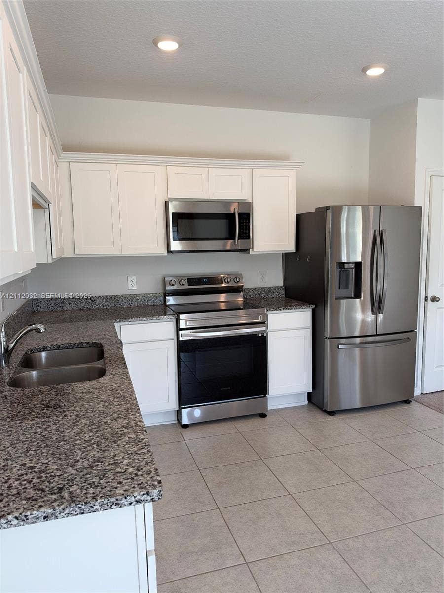 254 Mandovis Street, Davenport, Davenport, FL 33837 Kitchen featuring white shaker-style cabinetry, stone-finish countertops, stainless steel appliances, a double-basin undermount sink, and tile flooring