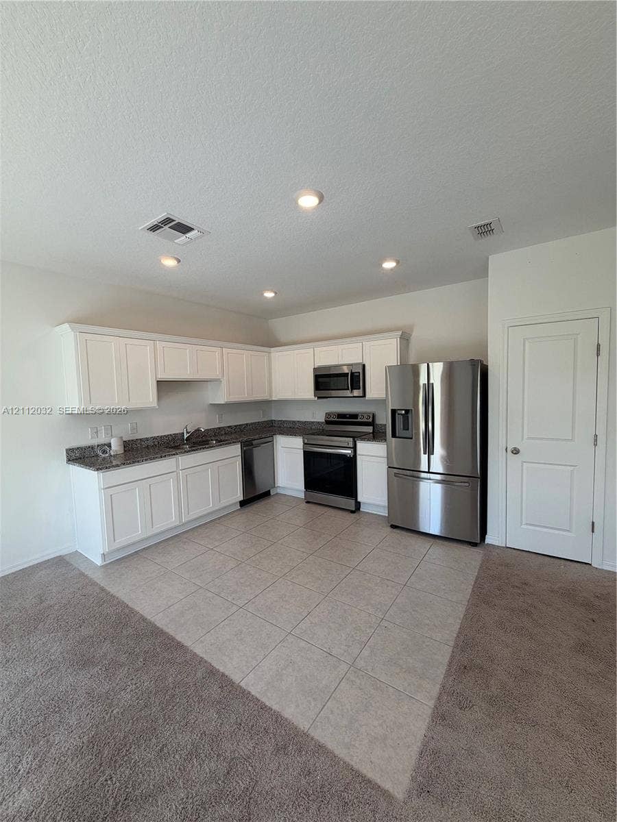 254 Mandovis Street, Davenport, Davenport, FL 33837 Kitchen featuring white cabinetry, stone-surface countertops, tile flooring, and stainless steel appliances including a refrigerator, range, and microwave