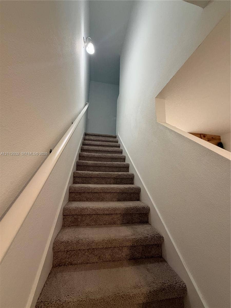 254 Mandovis Street, Davenport, Davenport, FL 33837 Carpeted staircase featuring a wall-mounted handrail, a sconce lighting fixture, and a recessed wall niche