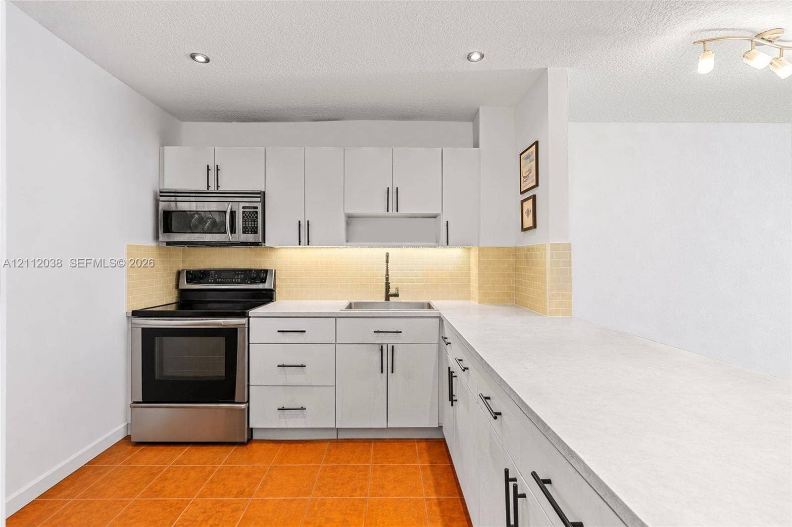 Kitchen featuring white cabinetry with matte black hardware, stainless steel range and microwave, light-toned stone-finish countertops, tile backsplash, and recessed lighting