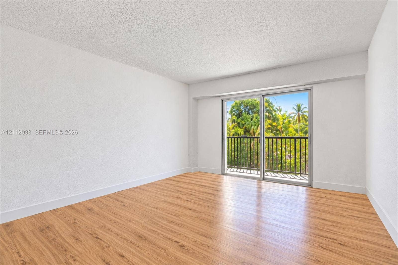 Neutral interior featuring wood-finish flooring, textured ceilings, and a sliding glass door providing access to a balcony with metal railing