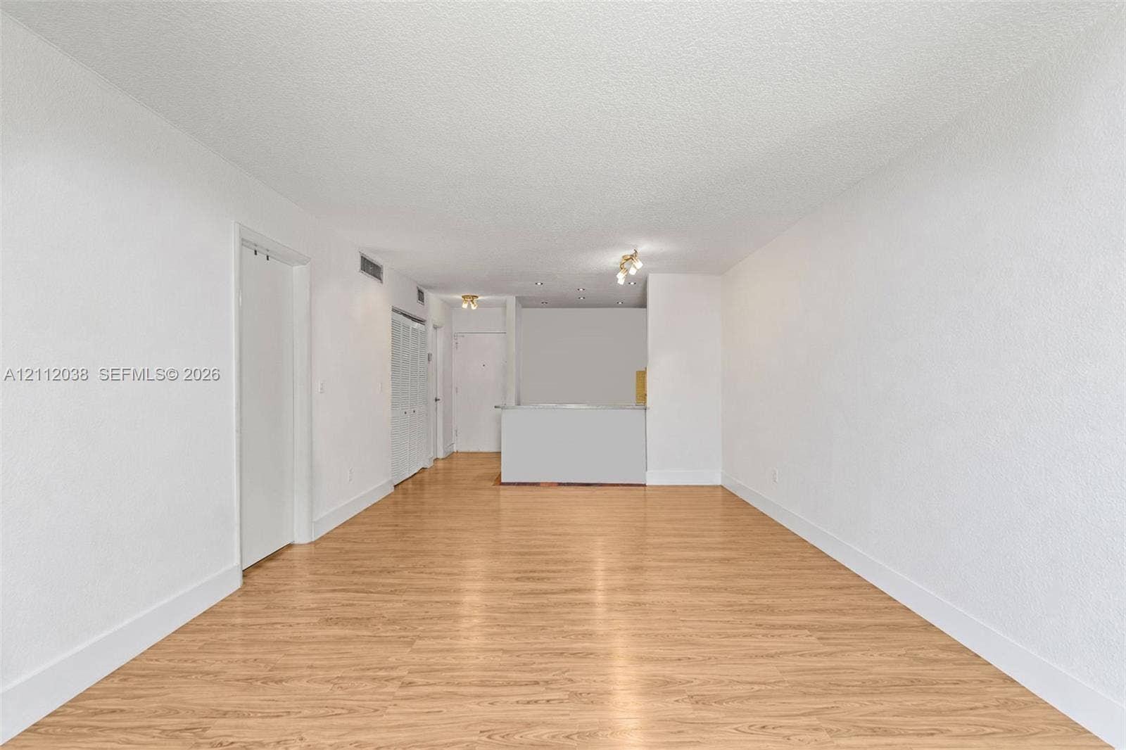 Open interior space featuring wood-finish flooring, textured ceiling, white walls, and built-in closet cabinetry