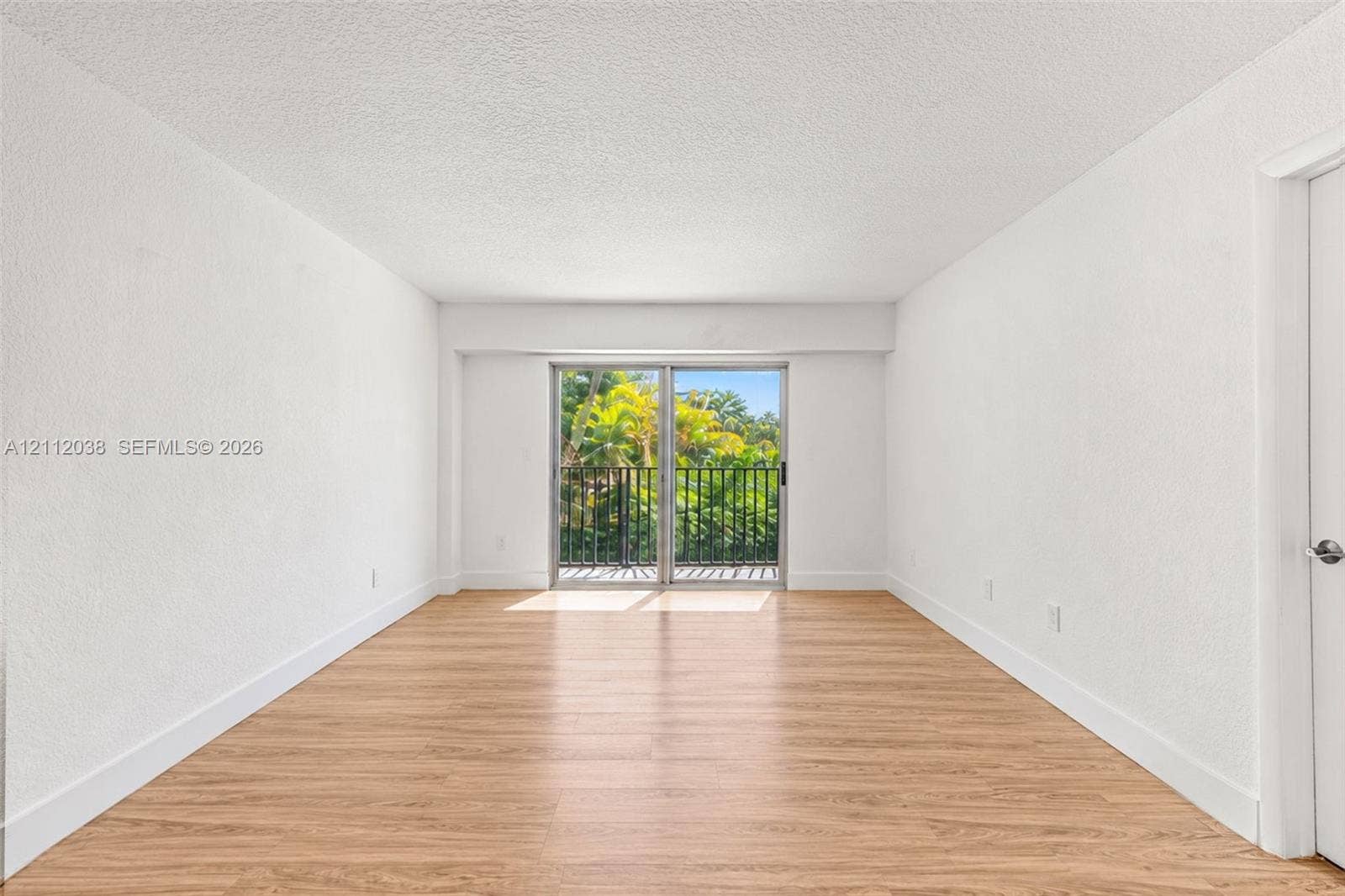 Interior space featuring wood-finish flooring, white walls, and a sliding glass door providing external access to a balcony with black metal railing