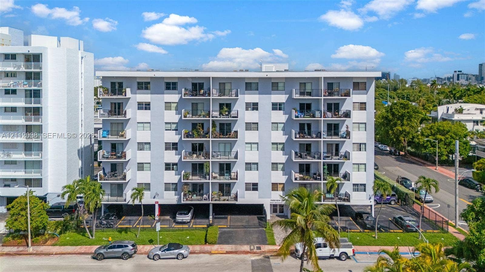 Multi-story residential building featuring reinforced concrete construction, private balconies, covered ground-level parking, and landscaped grounds with mature palm trees