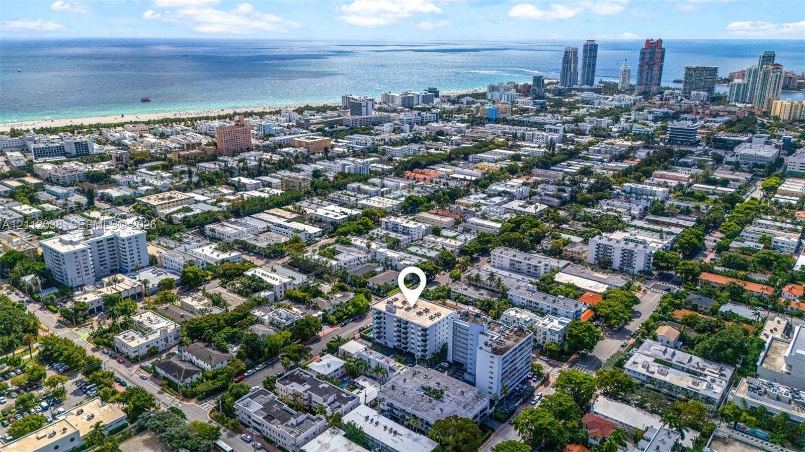 Aerial perspective of a multi-story residential building featuring a flat roof and white exterior facade, situated in an urban coastal setting