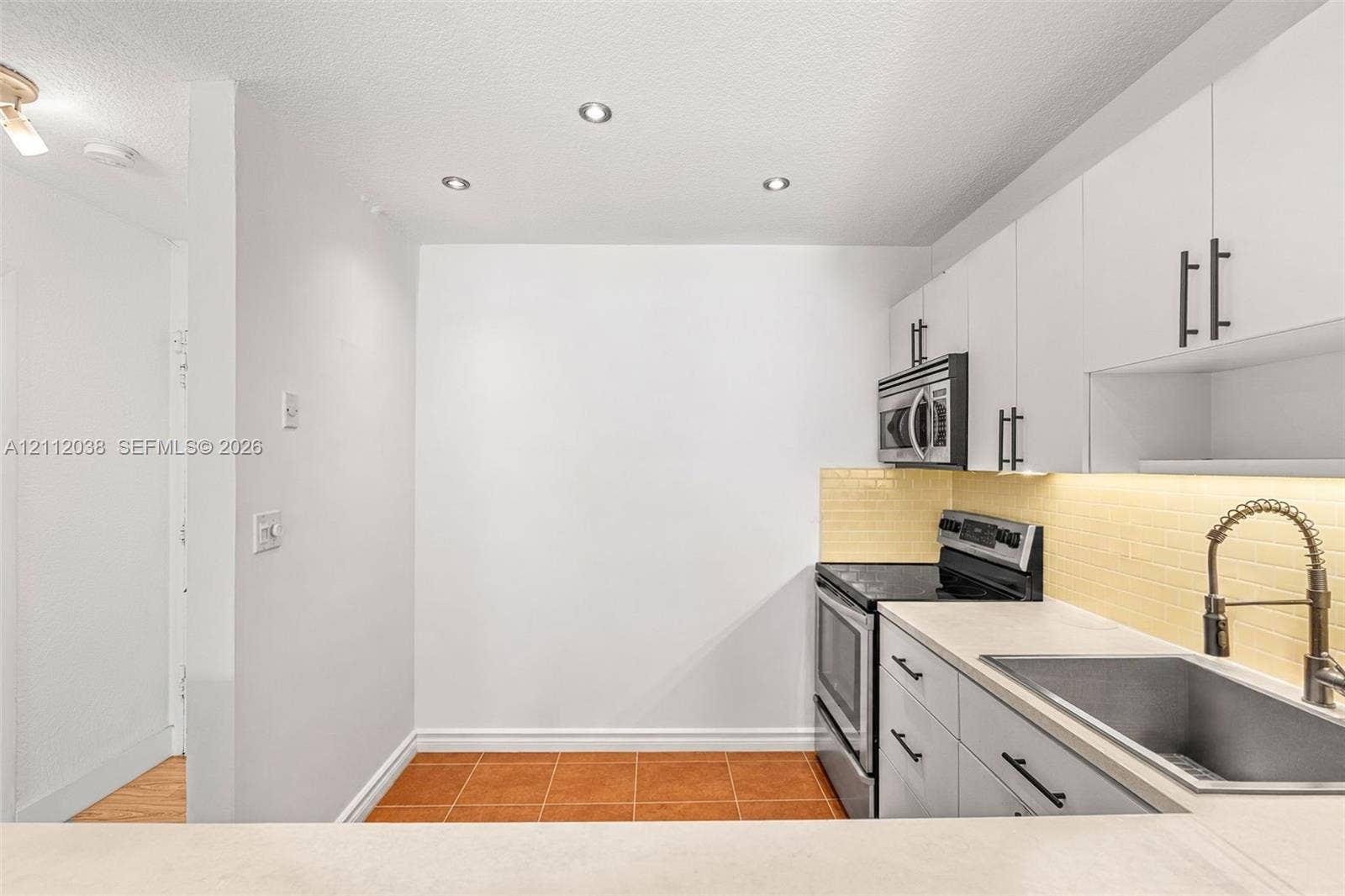 Kitchen featuring white flat-panel cabinetry, stainless steel appliances, a light-toned backsplash, a stainless steel sink with a high-arch faucet, and recessed lighting