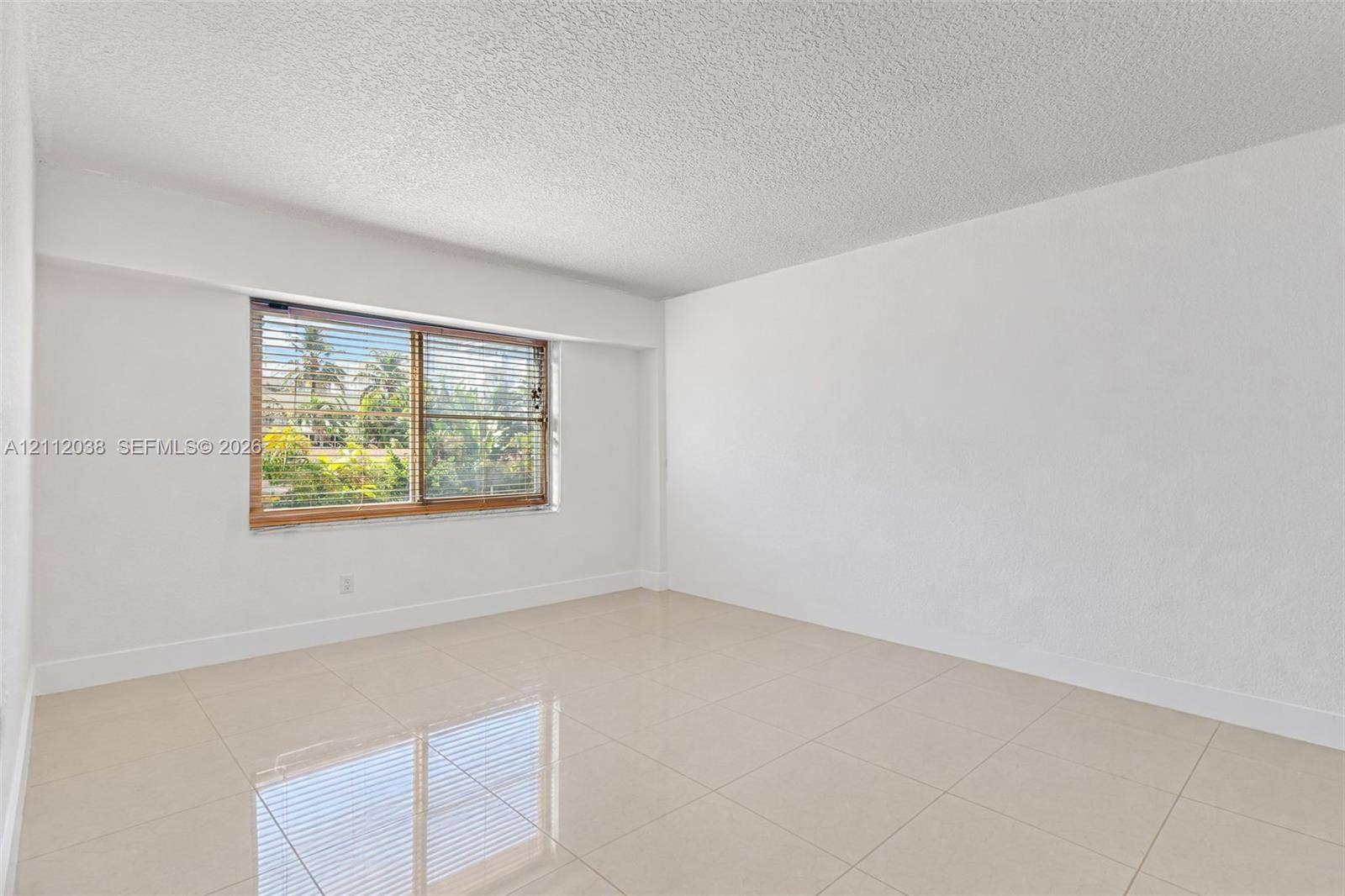 Interior space featuring light-colored tile flooring, smooth wall finishes, a window with integrated blinds, and textured ceiling finish