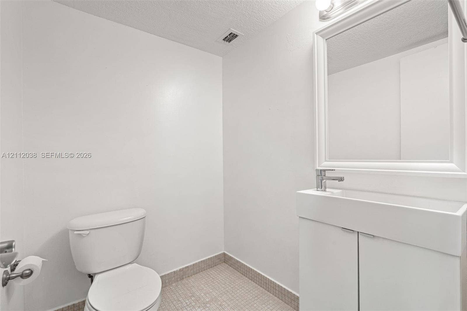 Half-Bathroom featuring a vanity with integrated sink, chrome faucet, framed wall-mounted mirror, and tiled flooring