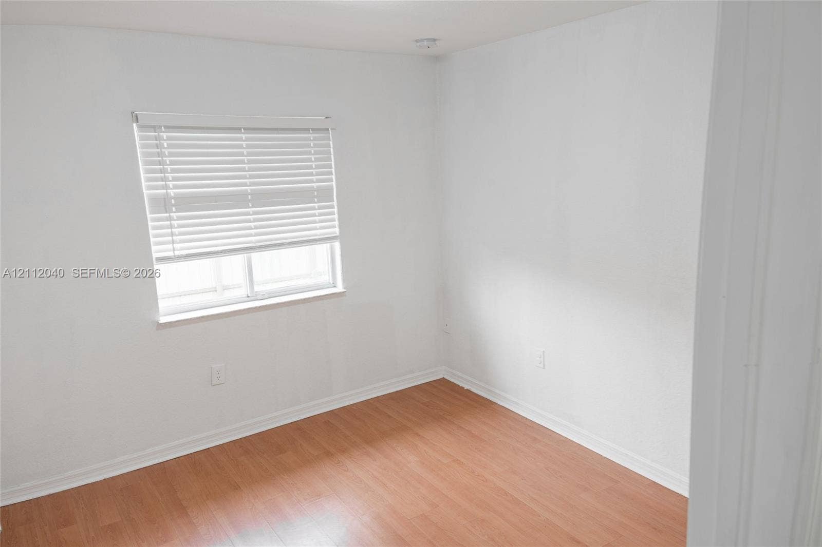 Interior space featuring wood-finish flooring, white walls, and a window fitted with horizontal blinds