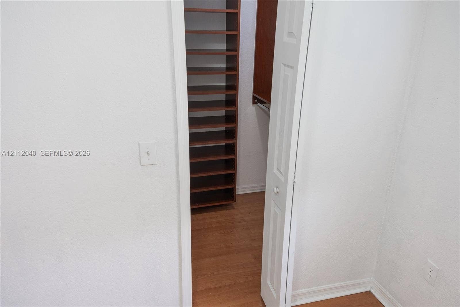 Walk-in closet featuring wood-finish flooring, built-in shelving, and a hanging rod, accessed by a bi-fold door