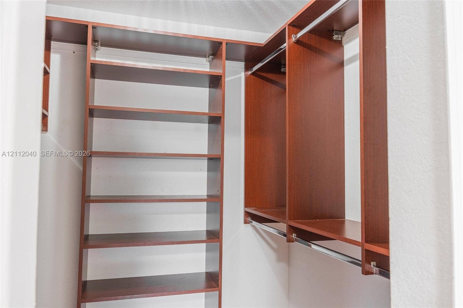 Walk-in closet featuring custom wood-finish shelving, overhead storage, and dual-level metal hanging rods