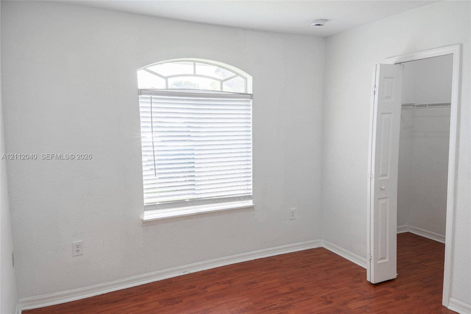 Room featuring wood-finish flooring, an arched window with horizontal blinds, and a built-in closet with double-panel doors