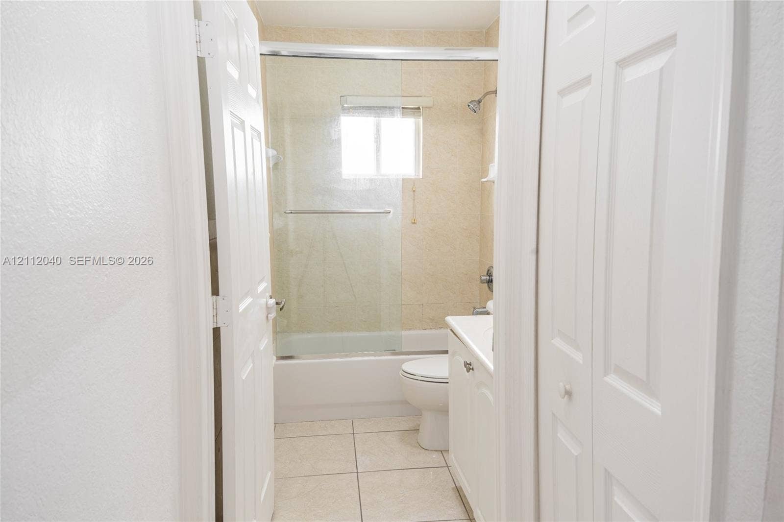 Bathroom featuring a tub-shower combination with a sliding glass enclosure, tile flooring, and a white vanity