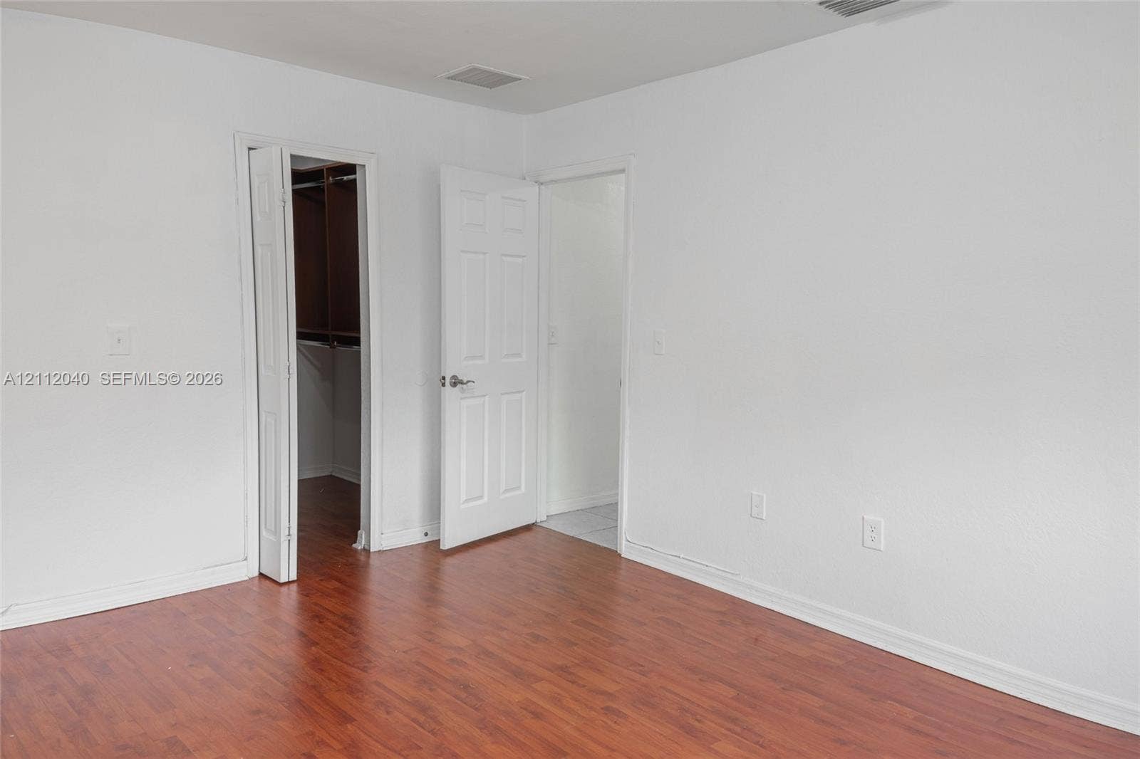 Wood-finish flooring, white paneled interior doors, and a built-in closet with hanging rods