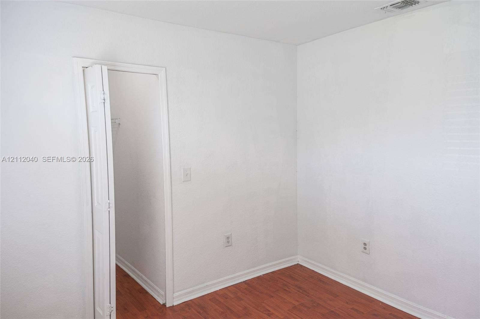 Room featuring wood-finish flooring, white walls, and a bi-fold closet door
