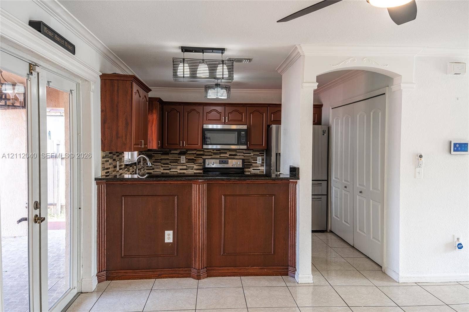 Kitchen featuring wood cabinetry, a decorative tile backsplash, stainless steel appliances, a raised breakfast bar, and tile flooring