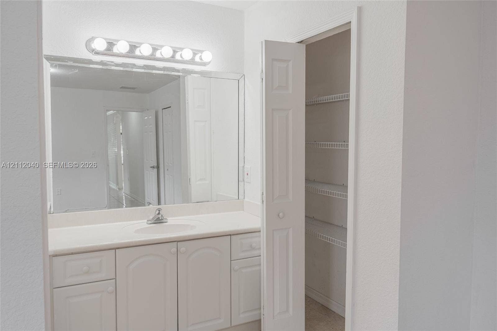 Bathroom featuring a white vanity with integrated sink, large wall-mounted mirror, six-light vanity fixture, and built-in closet with wire shelving