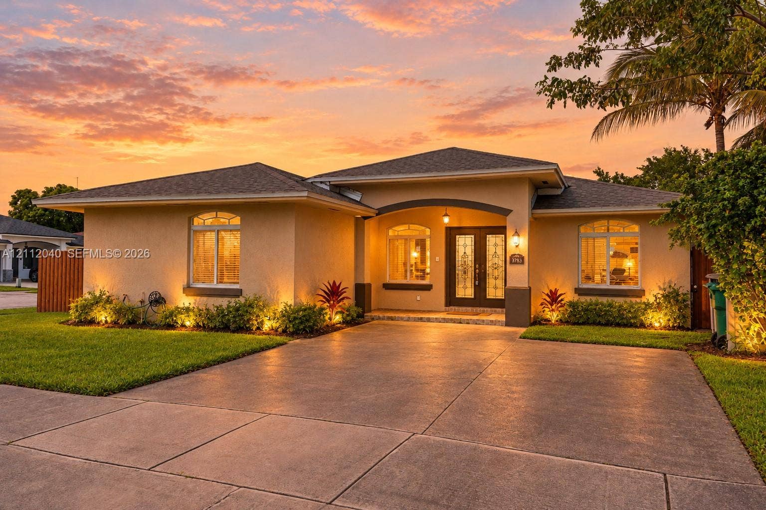 Stucco exterior residence featuring an arched covered entryway, double glass-panel front doors, a concrete driveway, and a shingle roof