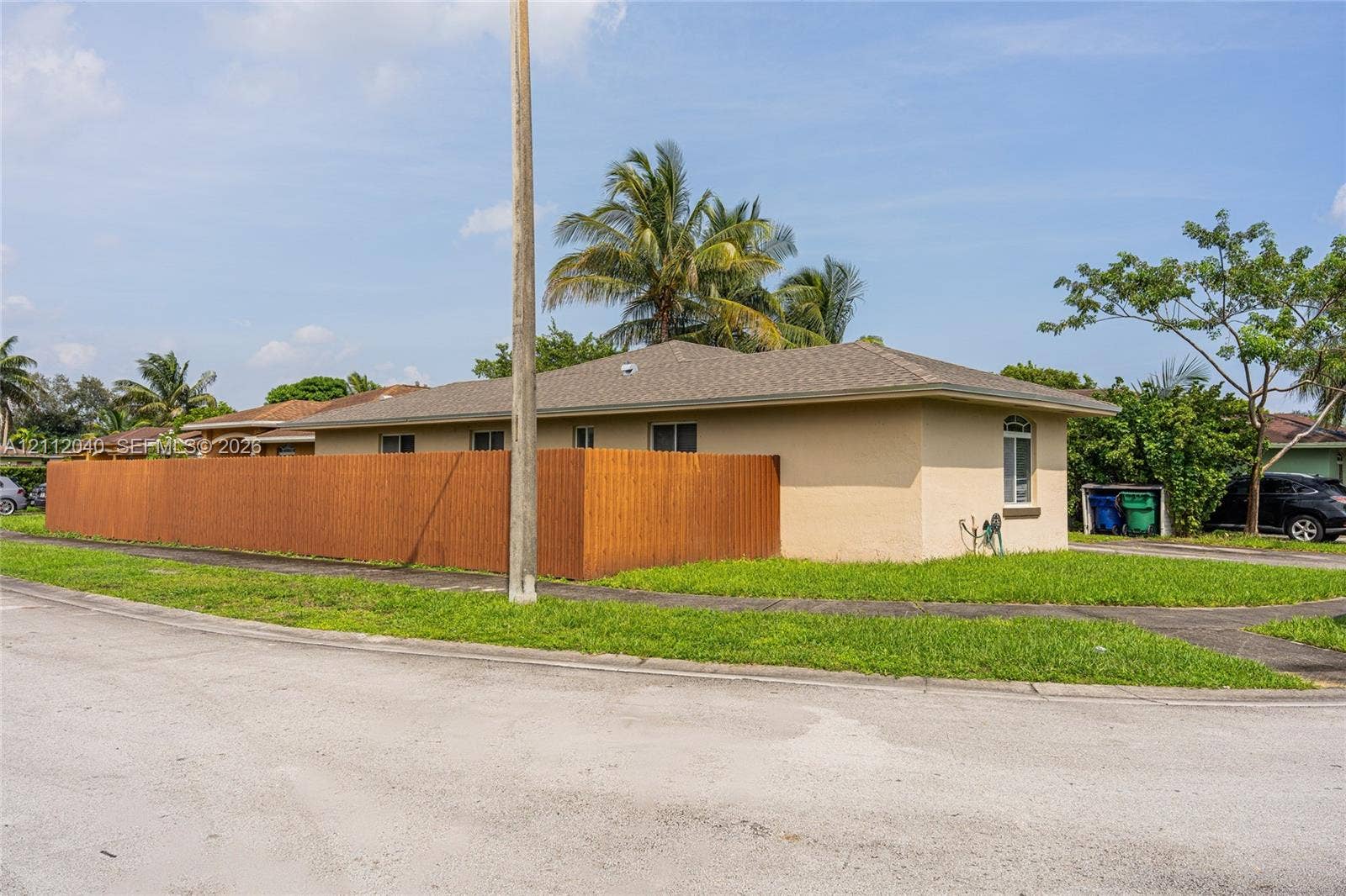 Single-story exterior with light-toned stucco siding, hip roof, arched window detail, and wrap-around wood privacy fencing