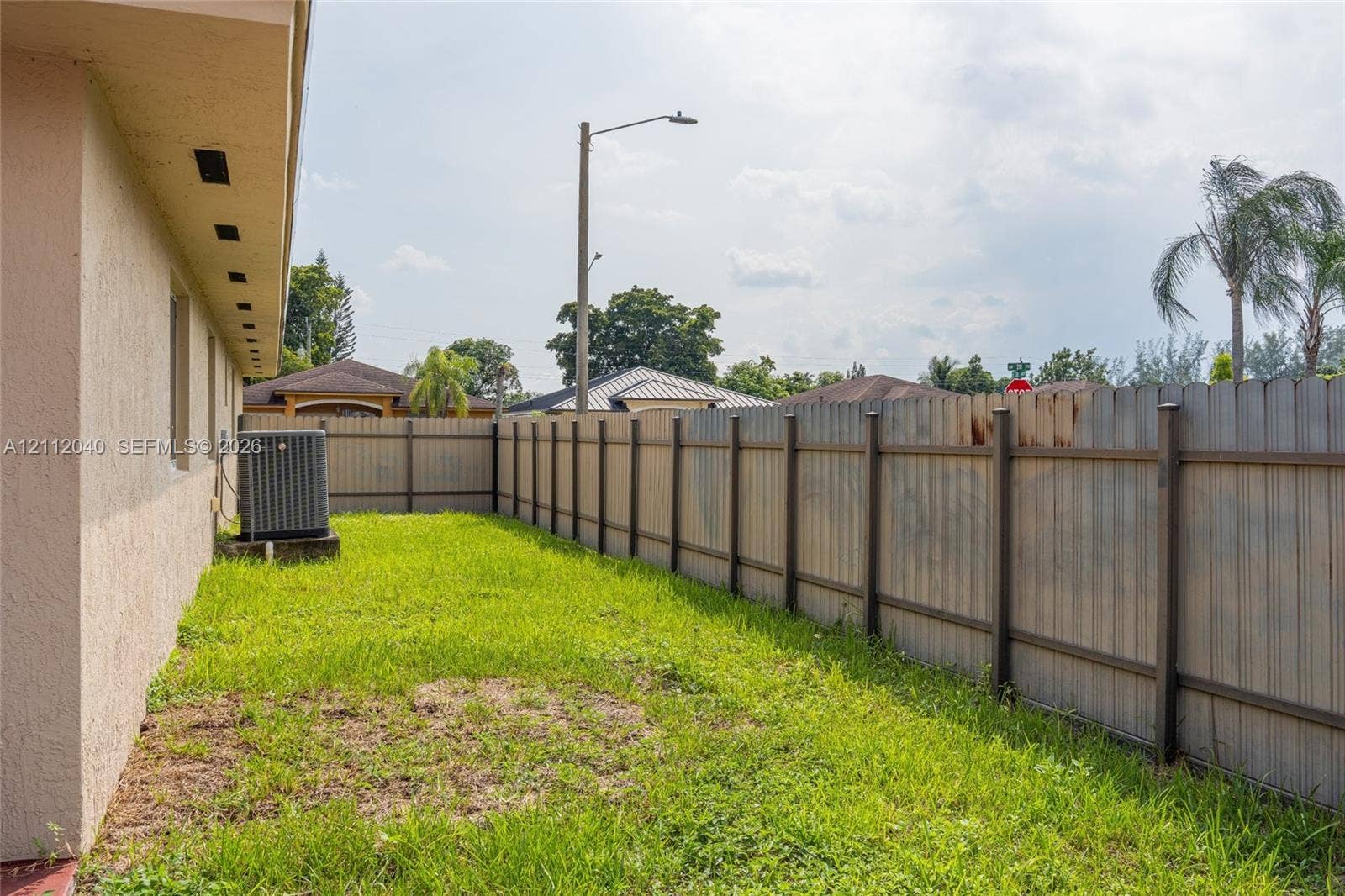 Side yard featuring stucco exterior wall, integrated HVAC condenser unit, and full-height perimeter wood fencing
