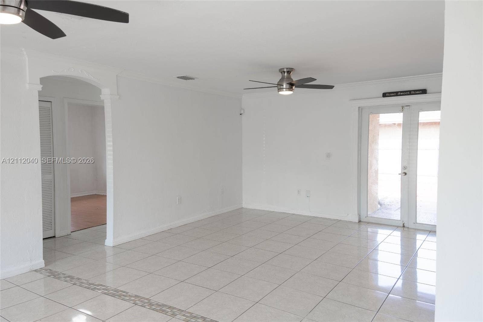 Interior space featuring large-format ceramic tile flooring, two multi-blade ceiling fans with integrated lighting, a decorative arched entryway, and double glass-paned doors