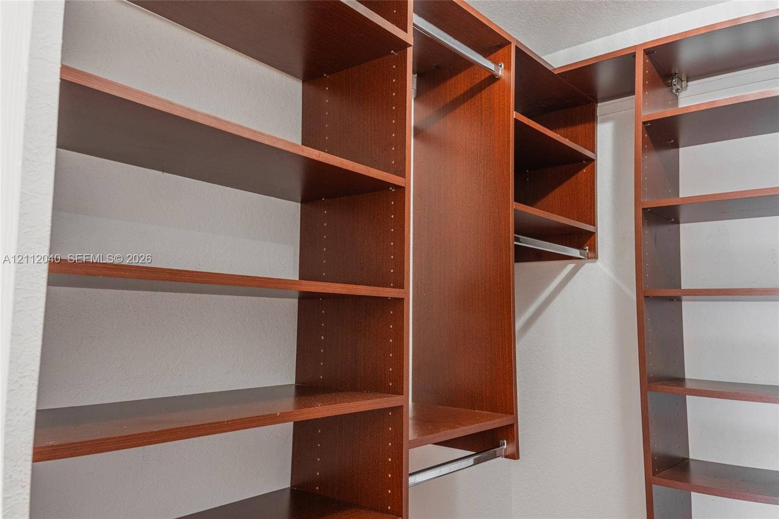 Custom walk-in closet featuring wood-finish cabinetry, adjustable shelving, and integrated metal clothing rods
