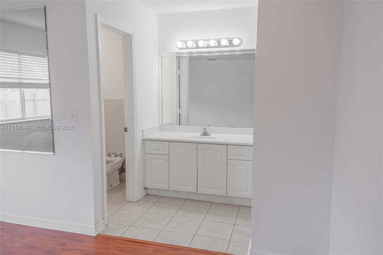 White vanity with storage cabinetry, solid-surface countertop, integrated sink, full-width mirror, and six-bulb vanity lighting